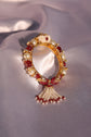 A gold-plated bangle adorned with pink polki, pearls, and ruby-colored stones, featuring a tassel design.