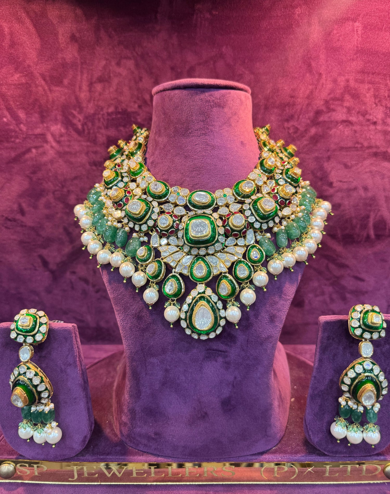 Green and gold necklace and earrings set on a purple stand with &