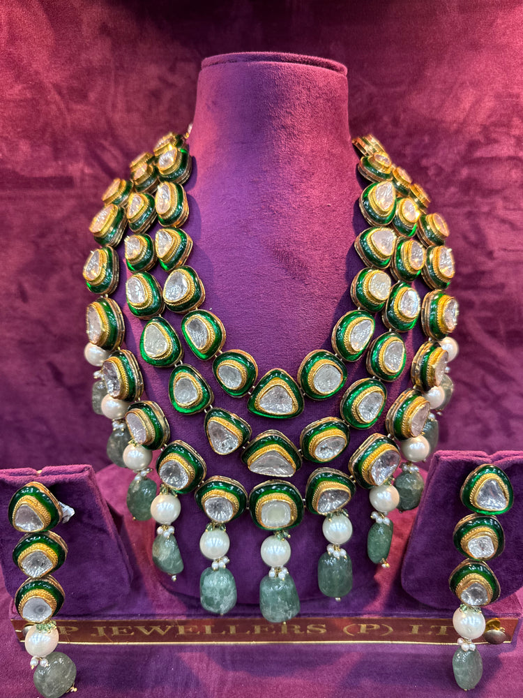 Green and gold necklace set on a purple stand with "SP. Jewellers" branding.