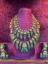 Green and gold Polki necklace with matching earrings on a purple stand against a pinkish-purple background "SP. Jewellers"