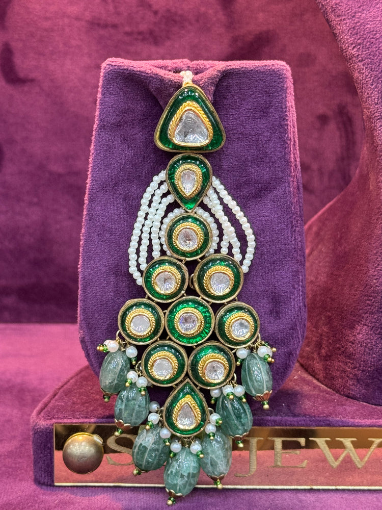 Decorative earring with green and gold elements on a purple velvet stand.