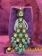 Decorative earring with green and gold elements on a purple velvet stand.